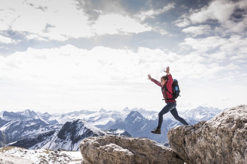 Climber leaping between summit rocks